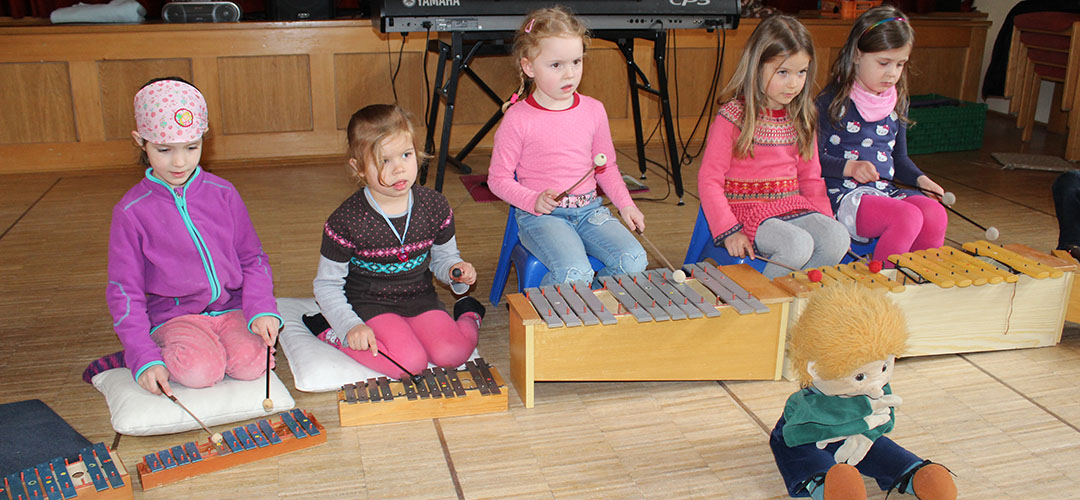 Slide05 musikalische Früherziehung, fünf Kinder zusammen mit Robinson spielen Orff-Instrumente